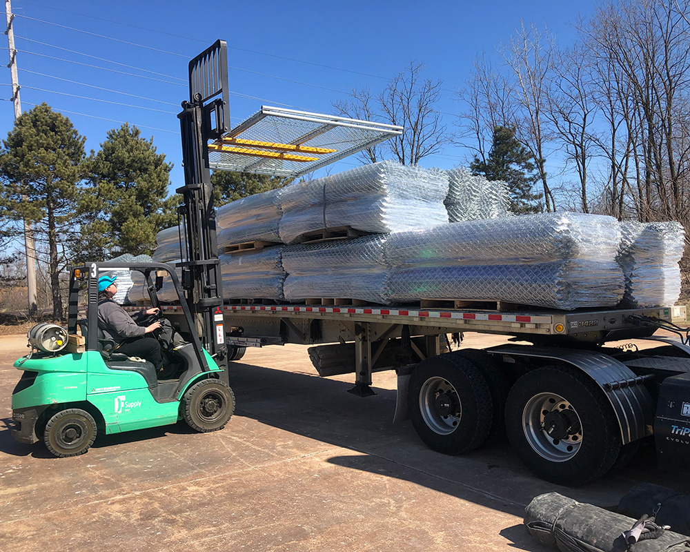 Man loading chain link fence section onto a truck bed with a forklift